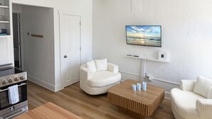 A modern living room with a wooden ceiling fan, a white couch, a wooden coffee table, and a flat-screen TV mounted on the wall. - Venice Villas Paradiso - Sunny - Pool (Venice)