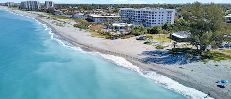 A coastal hotel with a beach view, multiple floors, and a mix of residential and commercial buildings in the background.