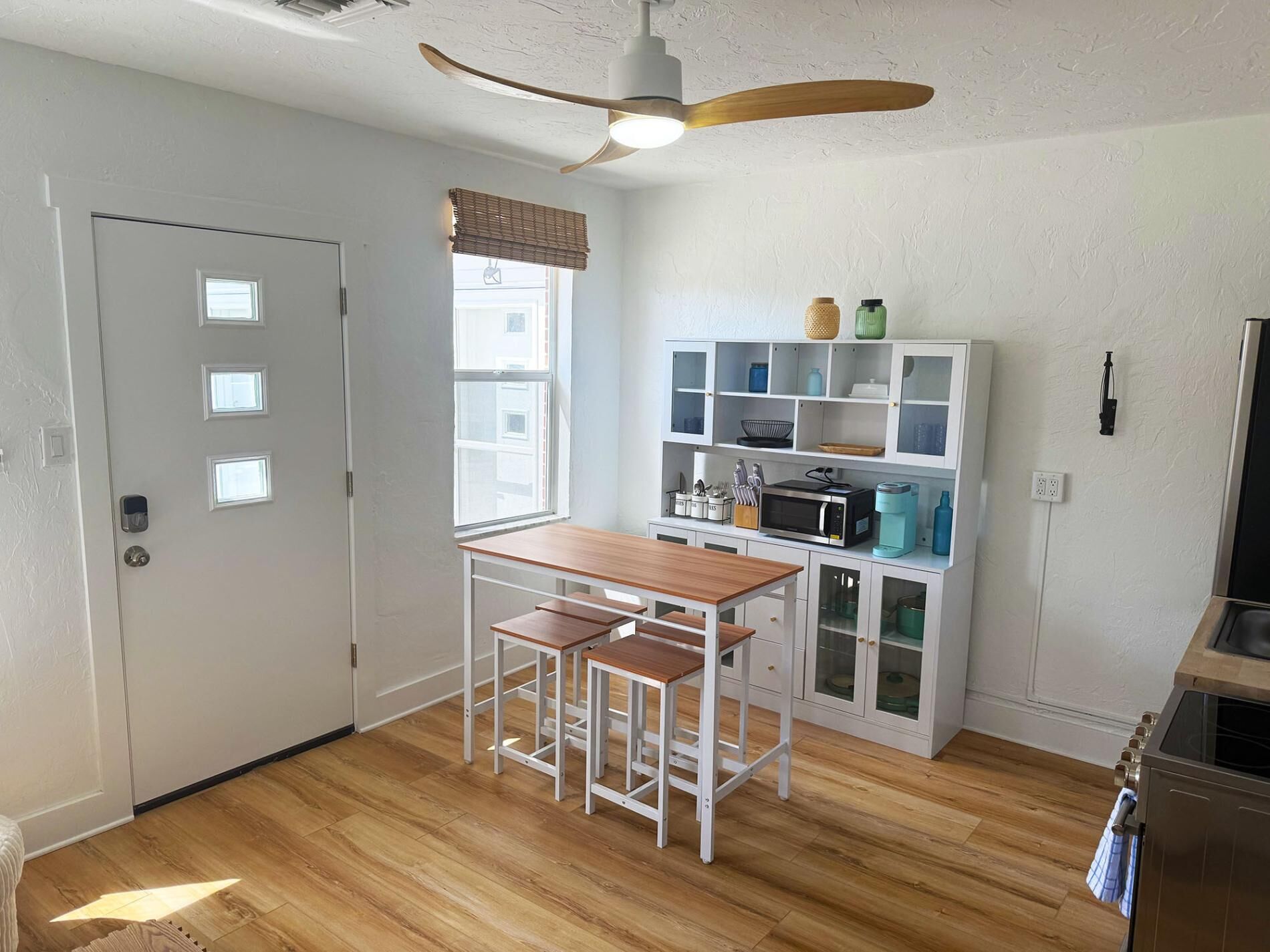 A compact kitchen with a wooden table and stools, a built-in microwave, and a ceiling fan.