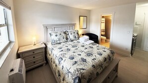 A bedroom with a bed, nightstand, lamp, ceiling fan, and a view of the bathroom. - Venice Villas Studio - Beachside - Pool (Venice)