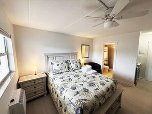 A bedroom with a bed, nightstand, lamp, ceiling fan, and a view of the bathroom. - Venice Villas Studio - Beachside - Pool (Venice)