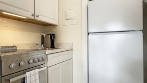 Een keuken met een roestvrijstalen fornuis, een witte koelkast en een koffiezetapparaat op het aanrecht.