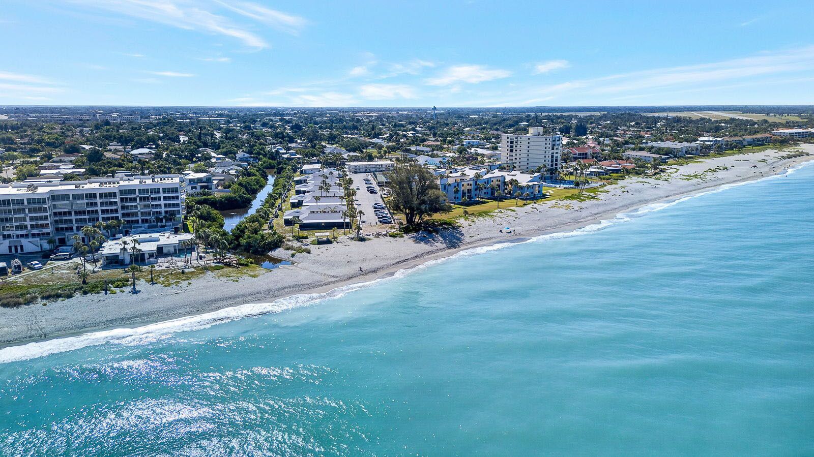 Une vue aérienne d’une zone côtière avec une plage, des bâtiments et un ciel dégagé.