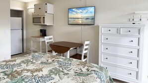 Een kleine kamer met een bed, een bureau, een magnetron en een televisie.
