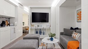Un saló modern amb televisió de pantalla plana, sofà gris, otomà i taula baixa amb una planta.