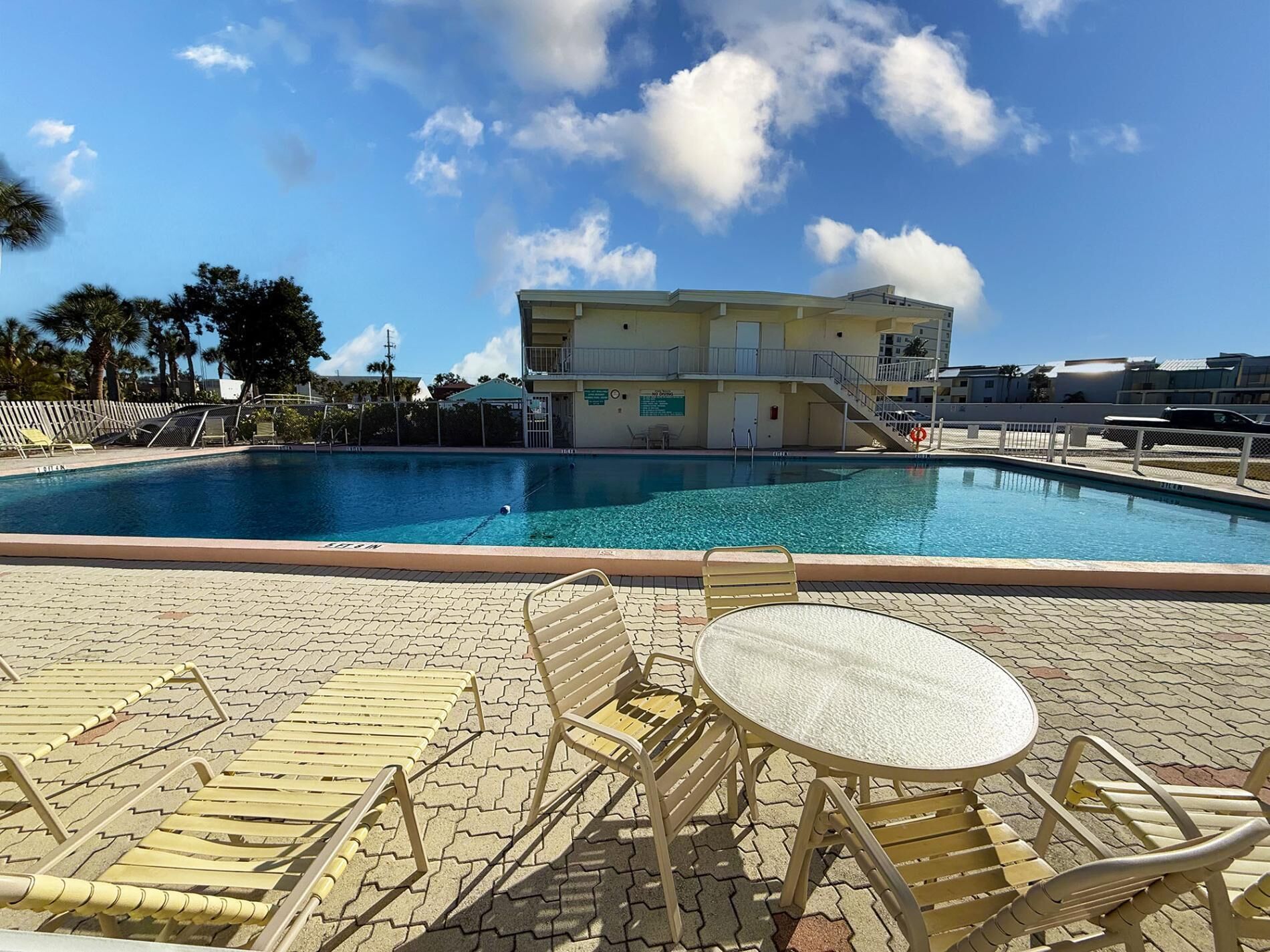 Una piscina con sillas de descanso y una mesa, rodeada por un edificio con balcón.