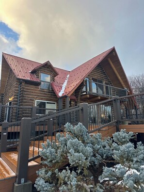 Une cabane en rondins avec un toit en métal, une terrasse en bois et un escalier menant à un balcon.