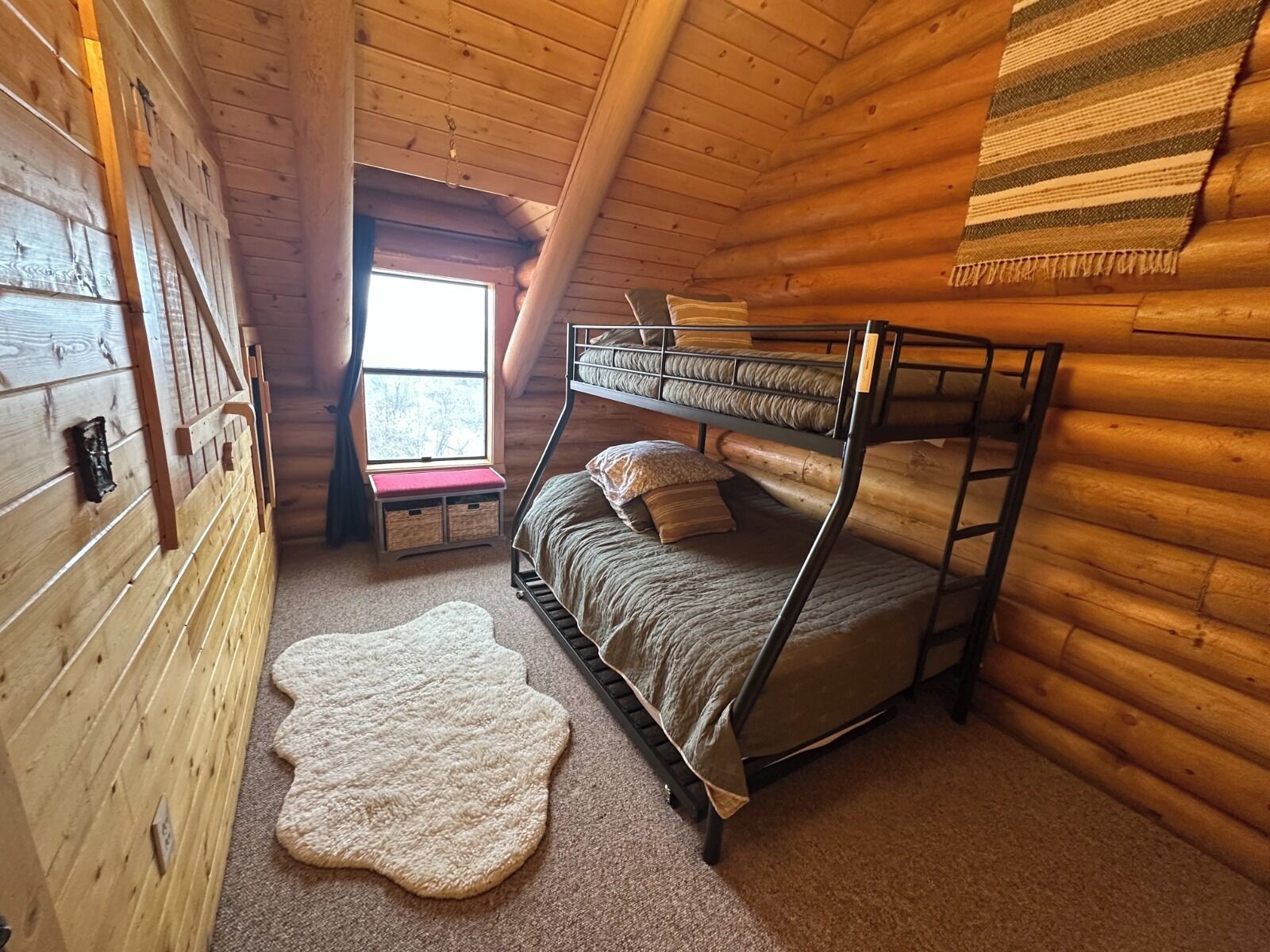 Una habitación tipo cabaña con literas, una ventana, un tapete y una pared de madera.