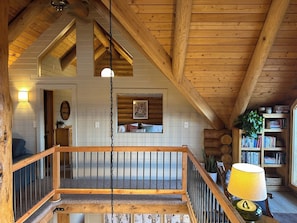 Un intérieur en bois avec un escalier, un luminaire suspendu, une bibliothèque et une fenêtre donnant sur un beau paysage.