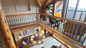 Ein großzügiger Loft-Raum mit hoher Decke, Holzbalken, einem Balkon mit Geländer und einem großen Fenster mit Aussicht.