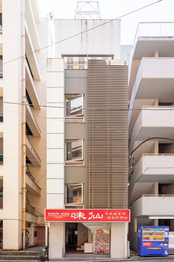 A multi-story building with a modern design, featuring a prominent vertical slatted facade and a ground-level entrance with a red sign. - Residence & Stay Hanzoumon (Tokyo)