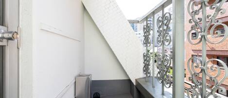 A balcony with a metal railing, a white wall, and a small trash bin.