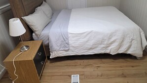Camera da letto con testiera in legno, comodino con lampada, letto con biancheria da letto bianca e finestra con tende.