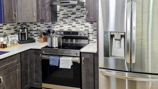 Una cocina moderna con armarios oscuros, un refrigerador de acero inoxidable, un horno empotrado y una cafetera.