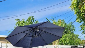Un jacuzzi con un paraguas negro, rodeado por una terraza de madera y una valla blanca.