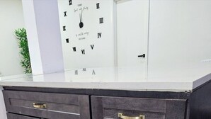 Una cocina con armarios oscuros, encimera blanca y un reloj en la pared.