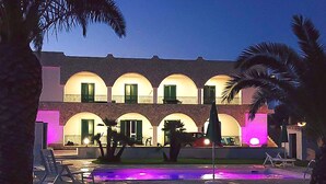 Un edificio con archi multipli e balconi, un'area piscina con giochi d'acqua e palme.
