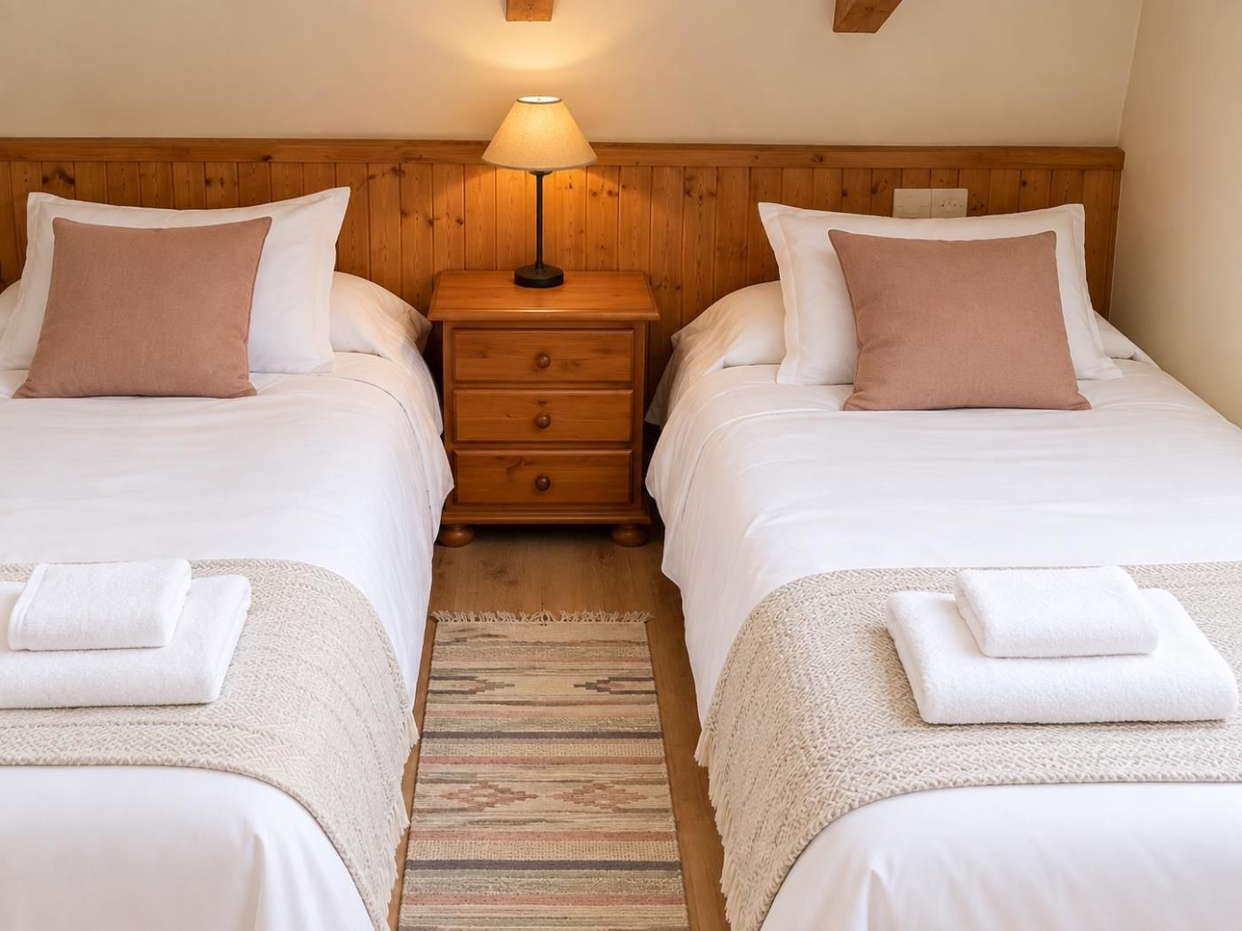 Une chambre d’hôtel avec deux lits, une table de chevet avec une lampe et un tapis à motifs.