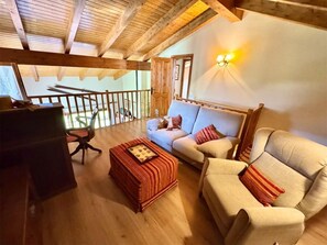Un salón acogedor con techo de madera, un sofá, una silla y una mesita.