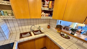 A kitchen with wooden cabinets, a tiled backsplash, a double sink, and a countertop with various items. - Duplex ideal for families, swimming pool, fireplace and Wi-Fi (Sainte-Léocadie)
