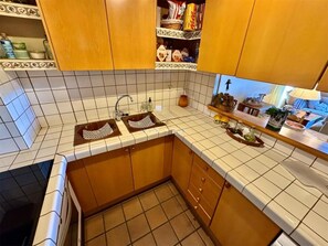 Una cocina con armarios de madera, salpicadero azulejado, pileta doble y encimera con diversos objetos.