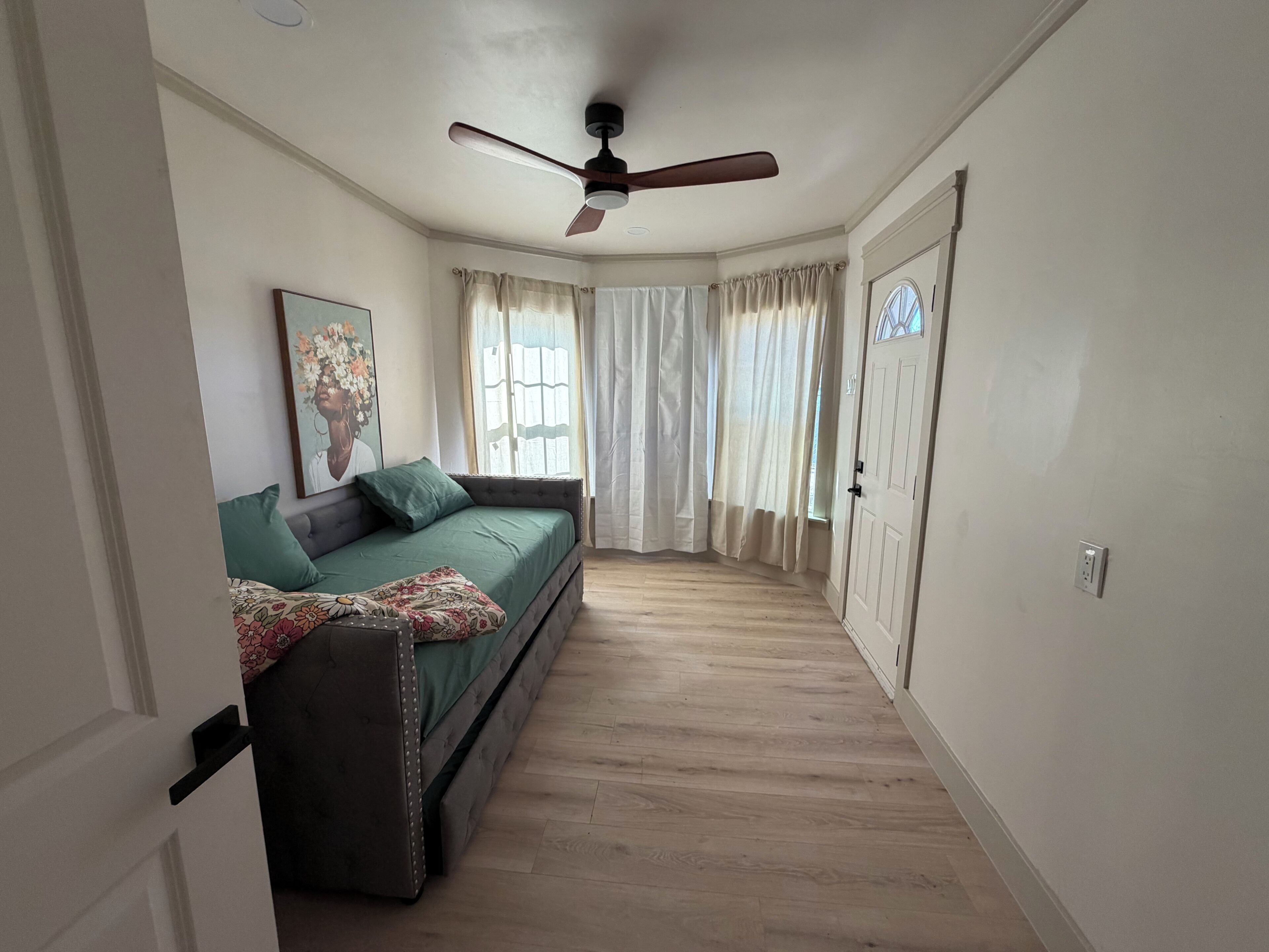 Une pièce avec un canapé, un ventilateur de plafond, une porte et une fenêtre avec des rideaux.