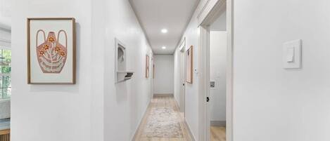 A hallway with framed artwork on the walls, a light-colored rug, and wooden flooring.