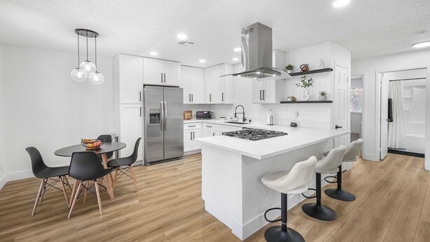 Una cocina moderna con armarios blancos, una isla central con taburetes de bar, un refrigerador de acero inoxidable y un horno empotrado.