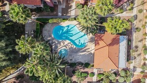 Vista aérea de un resort con piscina, palmeras y techo de tejas.