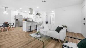 Un espacio habitable moderno, con decoración en blanco, que incluye una cocina, comedor y un sofá.