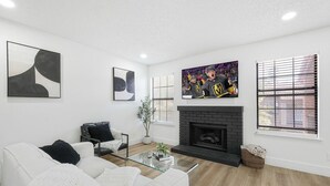 Una sala de estar moderna con un sofá blanco, una mesa de centro de vidrio, una chimenea y obras de arte en las paredes.