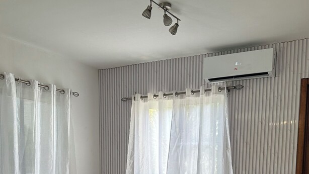 Uma sala de estar moderna com um sofá branco, pufes verdes, uma mesa de centro de vidro e um ar condicionado instalado no teto.