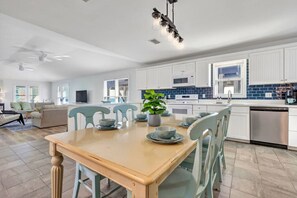 A modern kitchen with white cabinets, a wooden dining table, and a potted plant. - Sitt & Walk • New! 10 Steps to Beach • Gulf Views • Sleeps 8 (Gulf Shores)