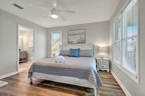 A bedroom with a bed, bedside lamps, a ceiling fan, and a painting on the wall. - Sitt & Walk • New! 10 Steps to Beach • Gulf Views • Sleeps 8 (Gulf Shores)