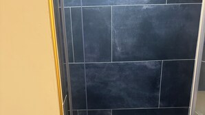 Zona de ducha con azulejos negros y suelo de cerámica.