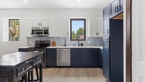 Una cocina moderna con armarios blancos, un refrigerador negro y una ventana con vistas a árboles.