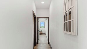 Un pasillo estrecho con suelo de madera, paredes blancas y una ventana a la derecha.