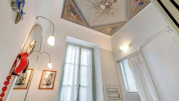 Une pièce dont le plafond est orné de motifs floraux, avec un grand miroir, un tableau encadré et une fenêtre avec des rideaux.
