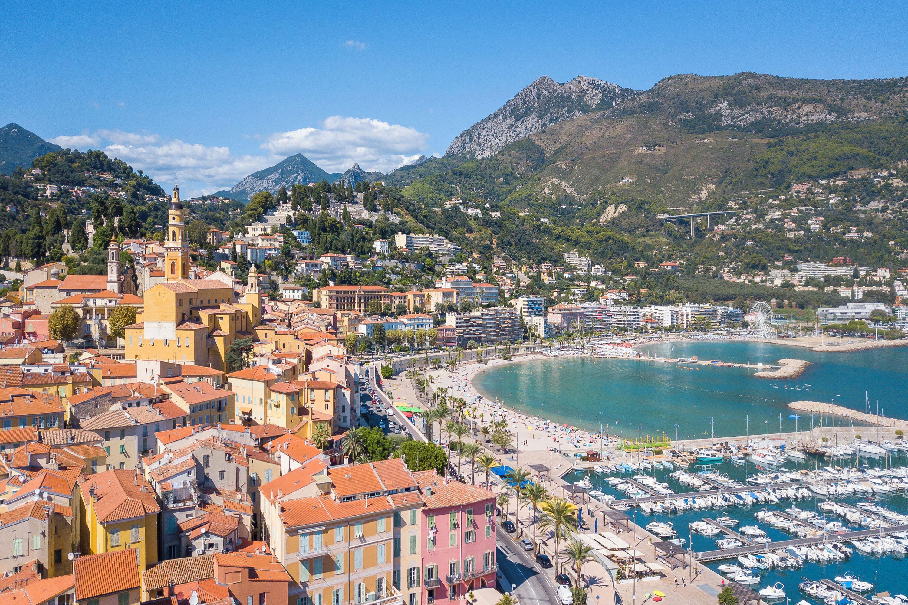 A coastal town with a marina, a church, and a mountain backdrop.