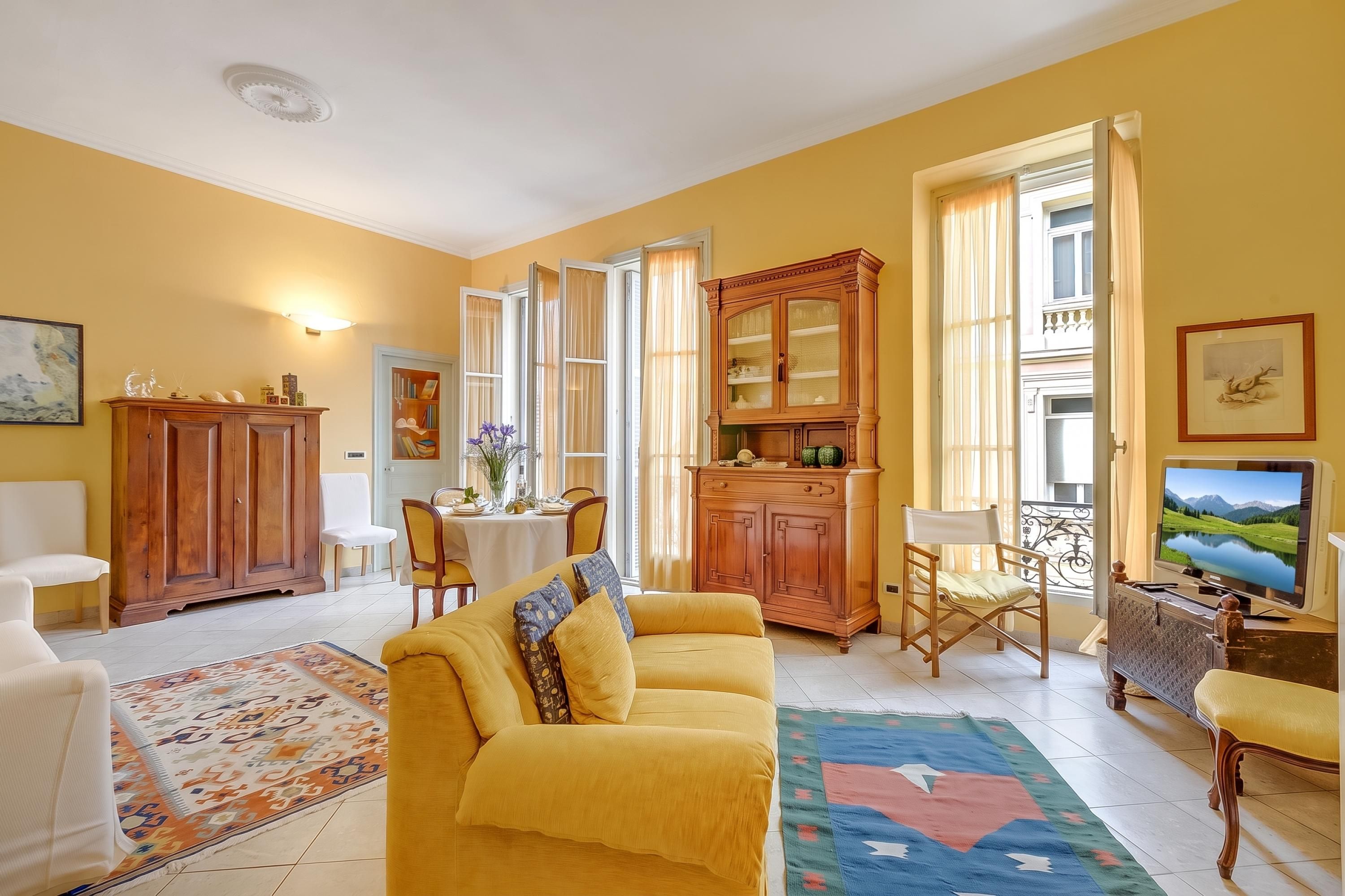 A living room with a yellow sofa, a dining table, and a television.