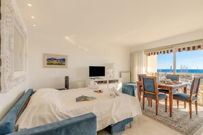 A hotel room with a bed, a TV, a dining table with chairs, a view of the sea, and a painting on the wall. - A Casa Di Arianna - Studio with Sea View Balcony, Menton, France (Menton)