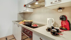 Een compacte keuken met een kookplaat, spoelbak en moderne apparaten, waaronder een koffiezetapparaat en een rode elektrische waterkoker.