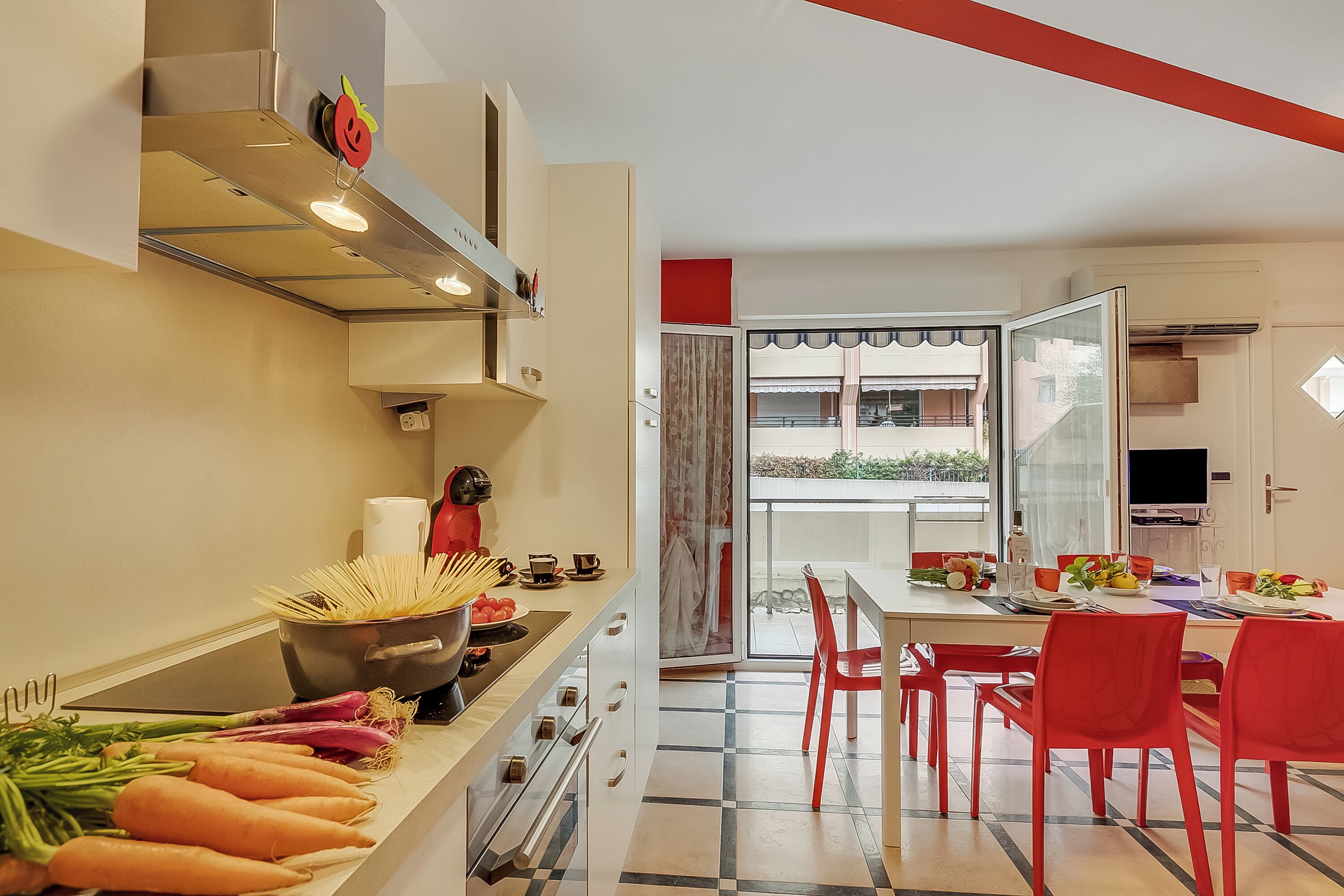 A modern kitchen with a dining area, featuring a pot of pasta, fresh vegetables, and a dining table set for four.