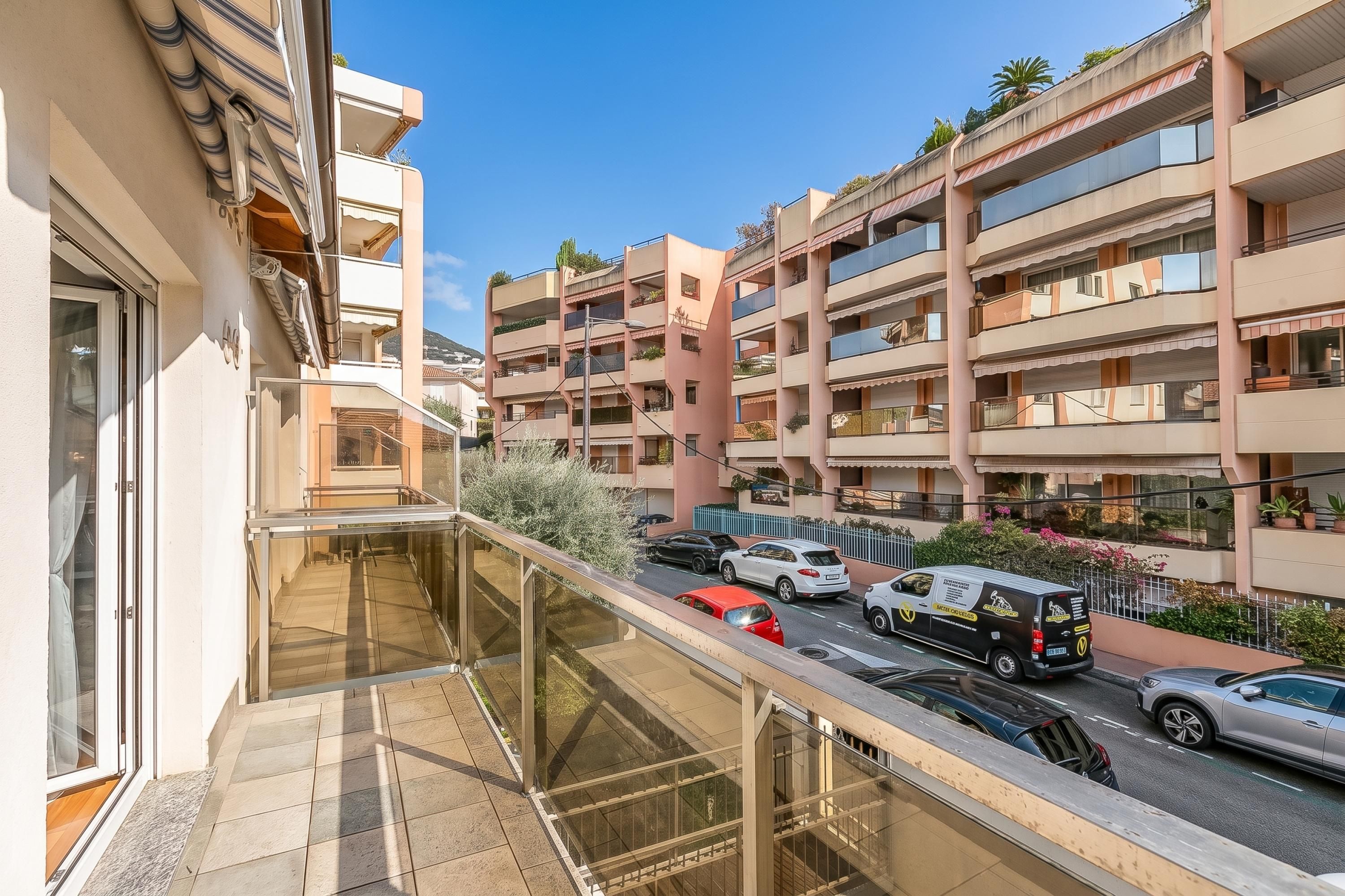 A residential building with multiple balconies, a street view with parked cars, and a clear sky.