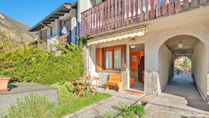 Ein Gebäude mit einer steinernen Fassade, einem hölzernen Balkon, Außenplätzen und einem Kiesweg, der zu einem Eingang führt.