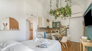 Una camera d'albergo moderna con un letto, una scrivania, un angolo ristoro e una piccola cucina.