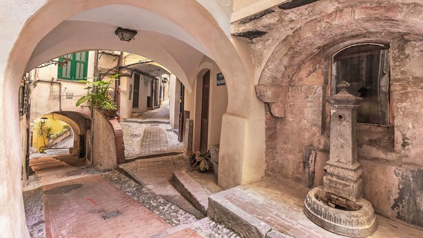 Un corridoio ad arco con una fontana, una scala e vista su una strada con edifici.