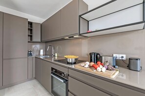 A modern kitchen with built-in appliances, a wooden cutting board with vegetables, and a kettle. - Glamour Apartment - Near Beach, Juan les Pins, France (Juan les Pins)