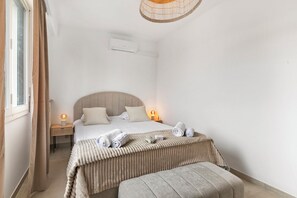 Un dormitorio con cama, lámparas de noche, mesita de noche, ventana con cortinas y aire acondicionado instalado en la pared.