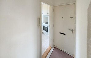 En gang med en hvid dør, en lille måtte og et kig på et køkken med skabe.